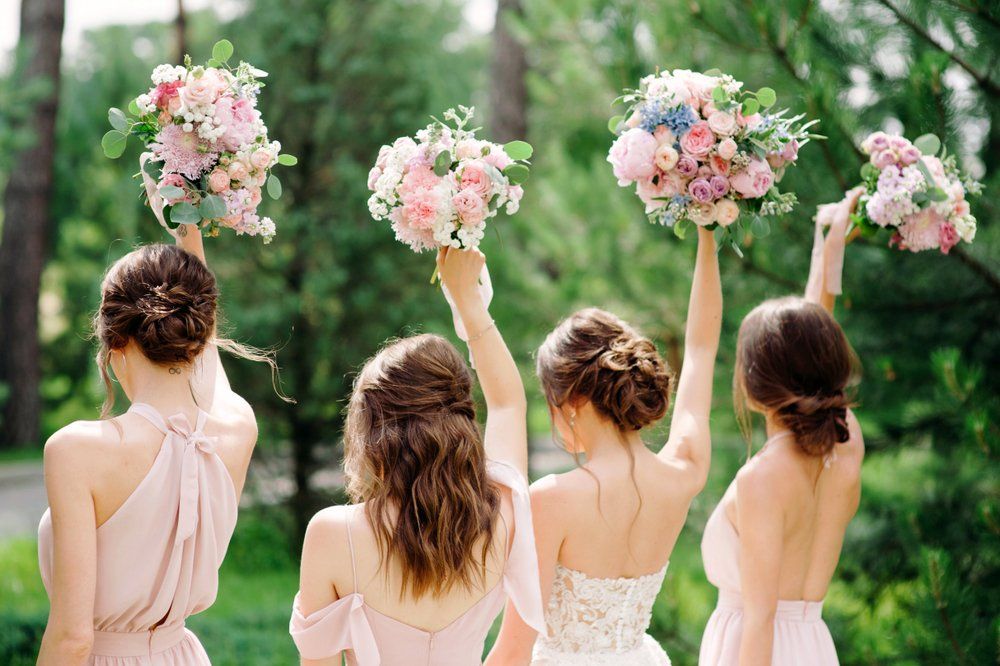 4 nő áll háttal a kamerának, virágcsokrokat emelnek az égbe esküvőn