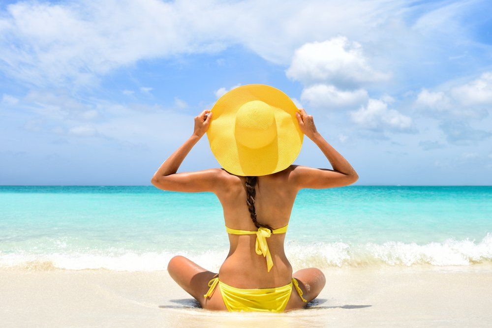 Nő sárga kalapban és fürdőruhában napozik a tengerparton