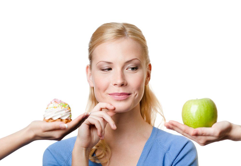Süteményt és almát nyújtó kezek között hezitáló nő