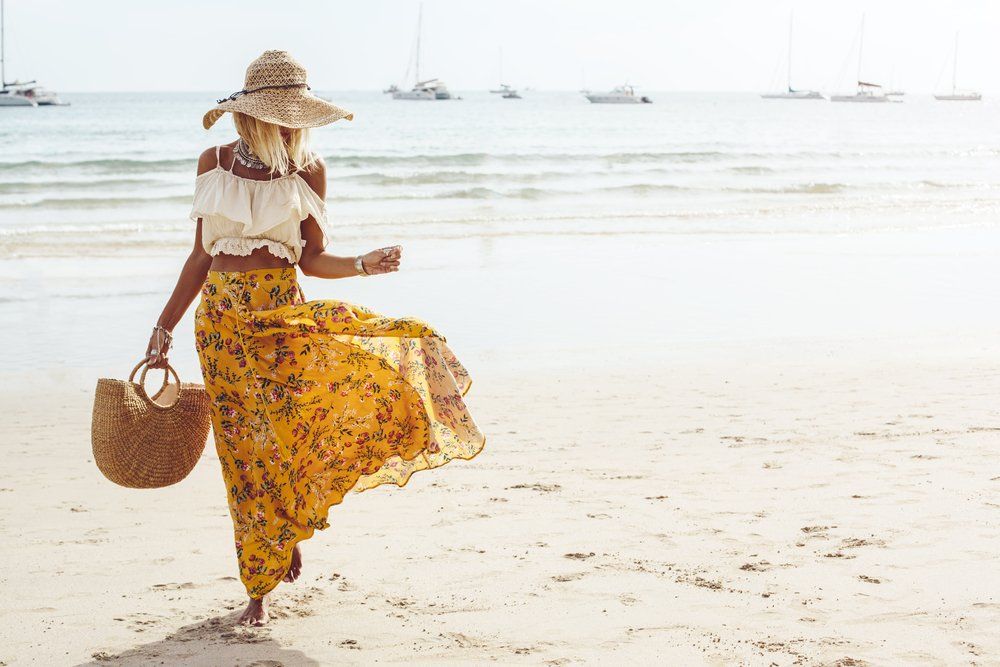 Fiatal szőke nő a tengerparton divatos ruhában sétál