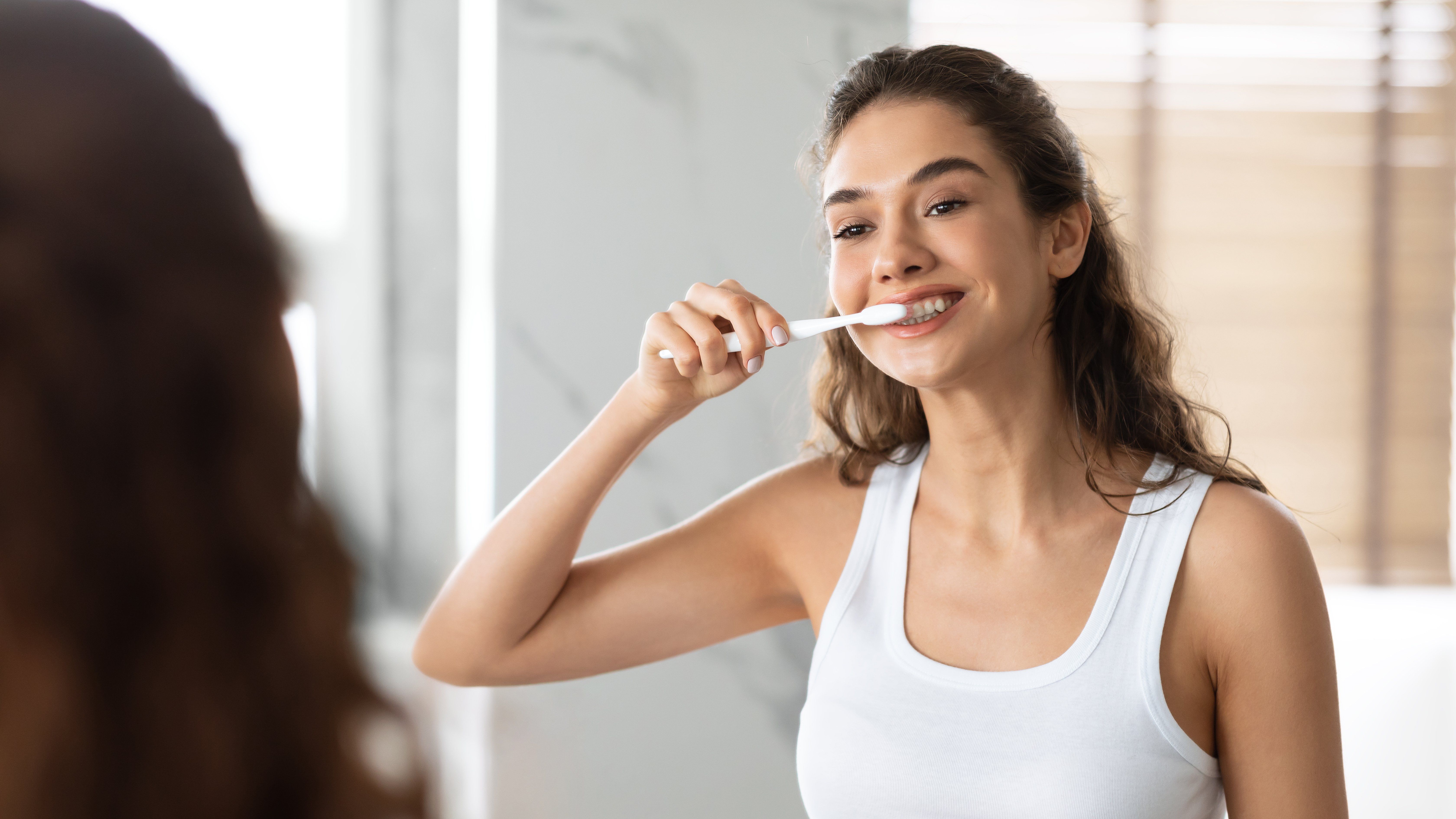egy fiatal nő mossa a fogát a tükör előtt