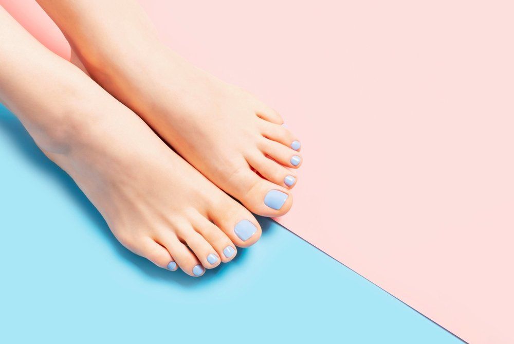 Pasztell kék színűre festett lábkörmű női lábak rózsaszín és kék háttéren