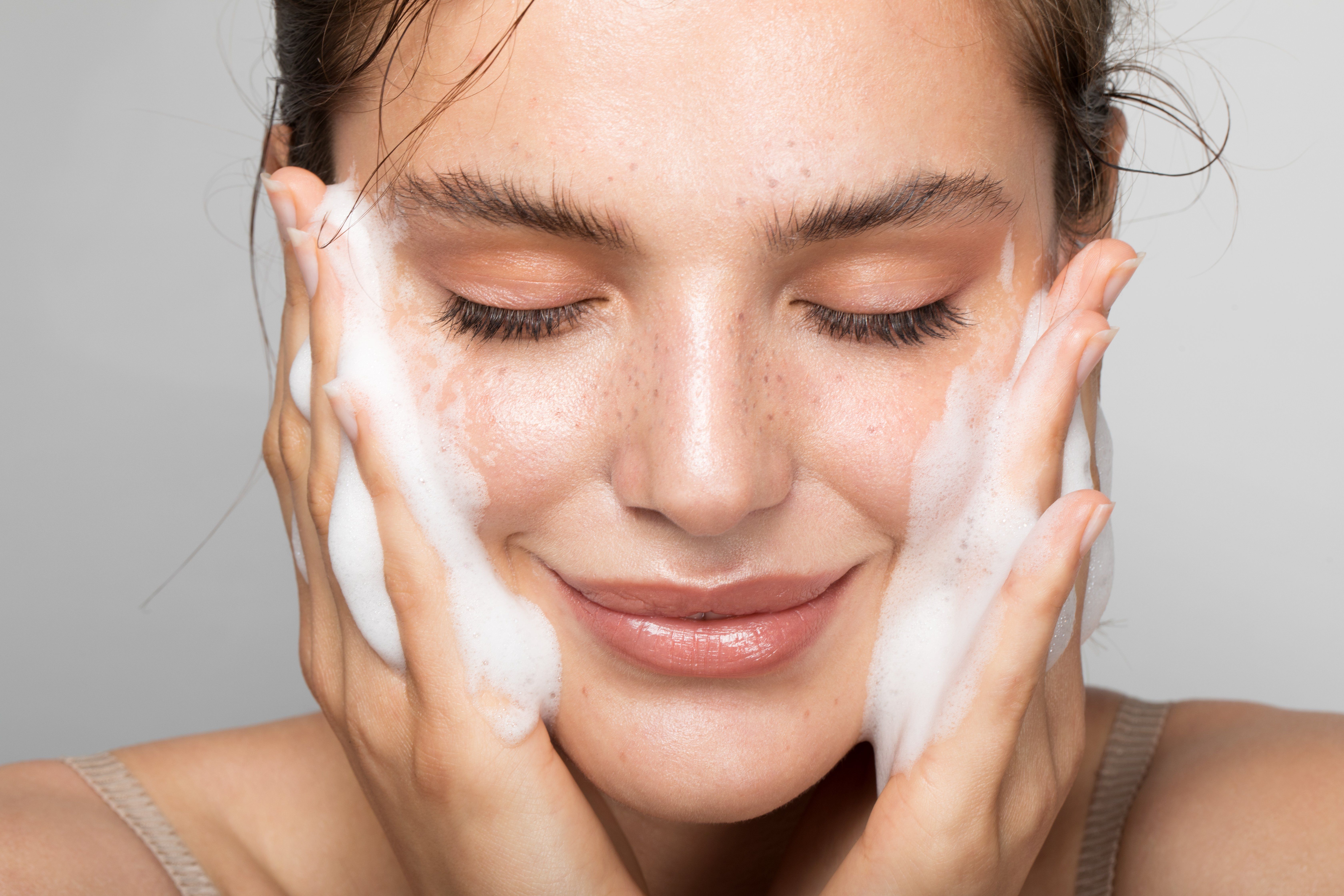 egy nő tisztítja az arcát habzó tisztítóval