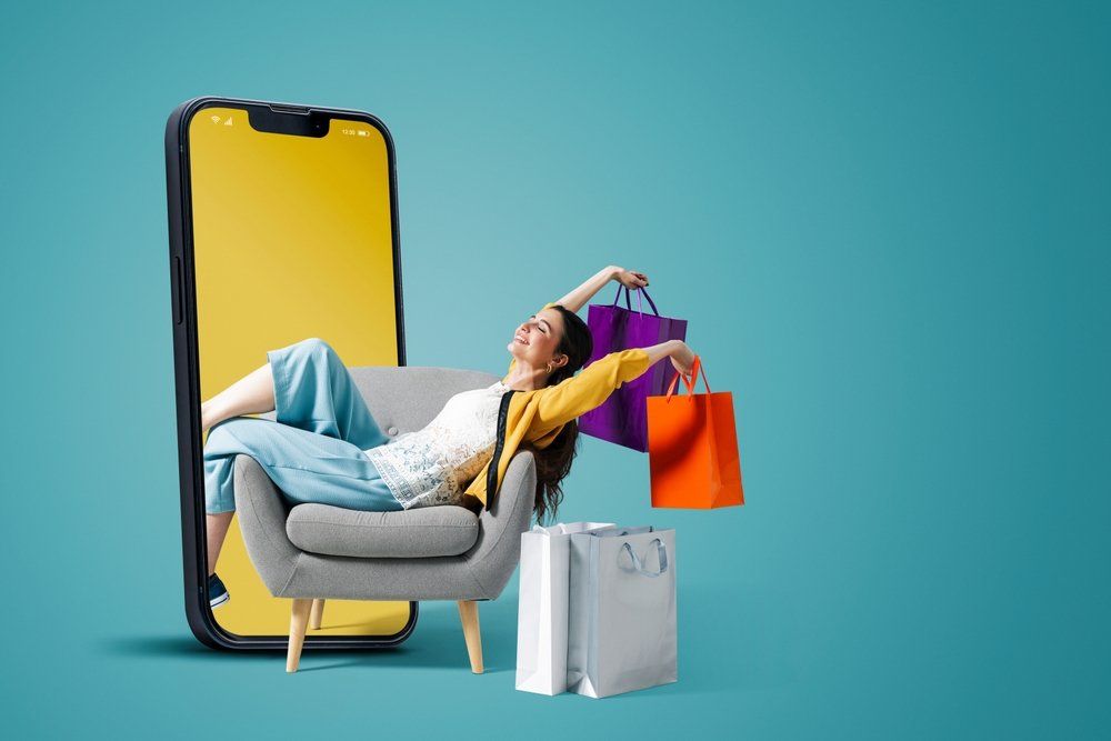Online vásárlás - mobiltelefon, mellette fotelban ülő nő, szatyrokkal