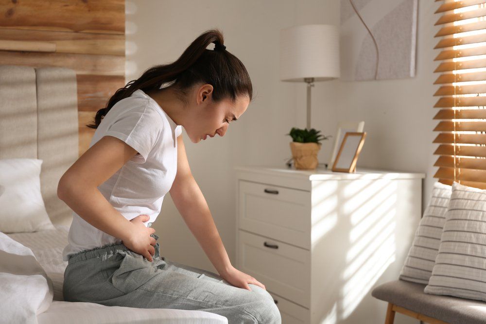 Gyomorfájástól szenvedő fiatal nő ül az ágyon