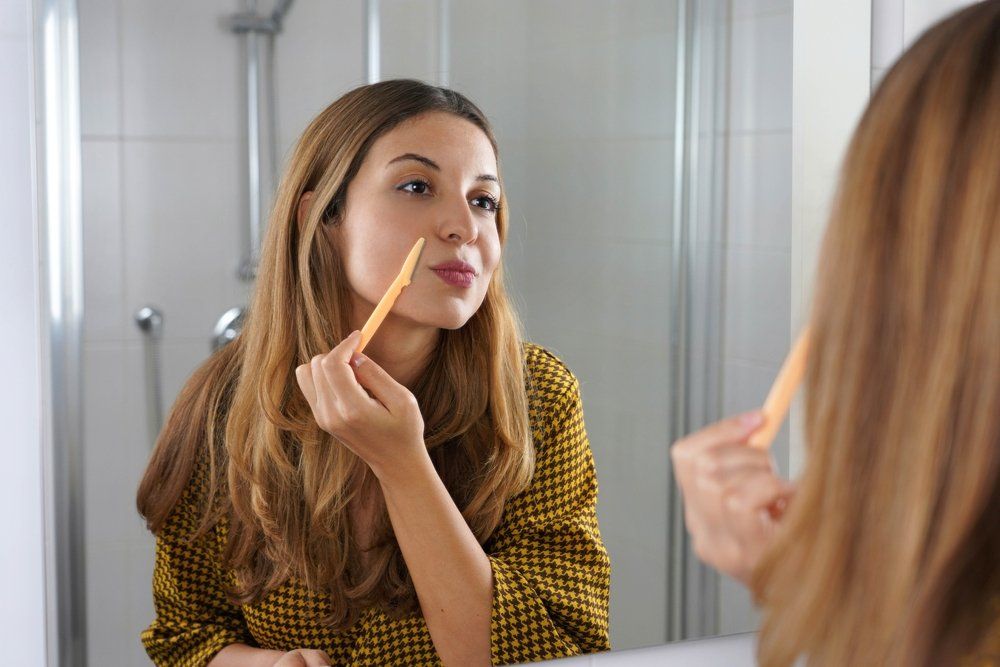 Arcszőrzetét borotváló nő a tükör előtt