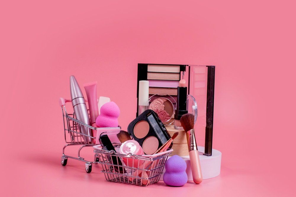 Kozmetikumok mini bevásárlókocsiban és kosárban, rózsaszín háttér előtt