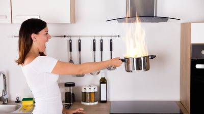 ijedt nő egy égő lábast tart a kezében a konyhában