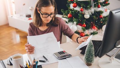 Nő a gép előtt olvas és számológéppel ad össze, karácsonyi dekoráció