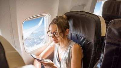 Nő ül a repülőgépen az ablak mellett és a telefonját nézi