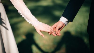 Férj és feleség fogják egymás kezét az esküvőjükön