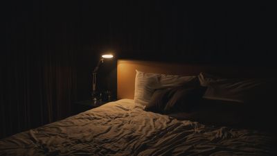 Egy éjjeli lámpa világít az ágy mellett