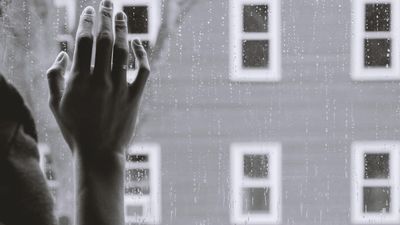 egy női kéz az ablakot támasztja miközben odakint esik az eső