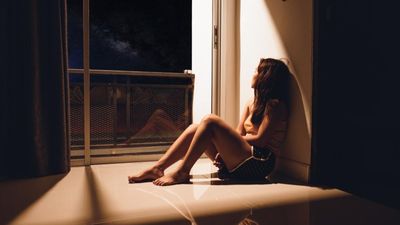 Egy lány egyedül ül az ablaka előtt