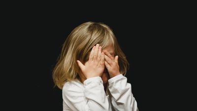 Egy szomorú kislány kezeivel takarja az arcát