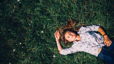Egy szőke hajú lány csukott szemmel fekszik a fűben