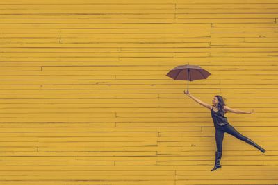 Egy boldog lány esernyővel a kezében egy sárga fal előtt
