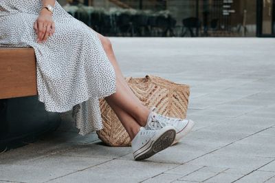 Fehér tornacipőt és pöttyös ruhát viselő nő ül egy padon nyáron