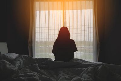 Nő ül egyedül az ágy szélén, néz ki az ablakon